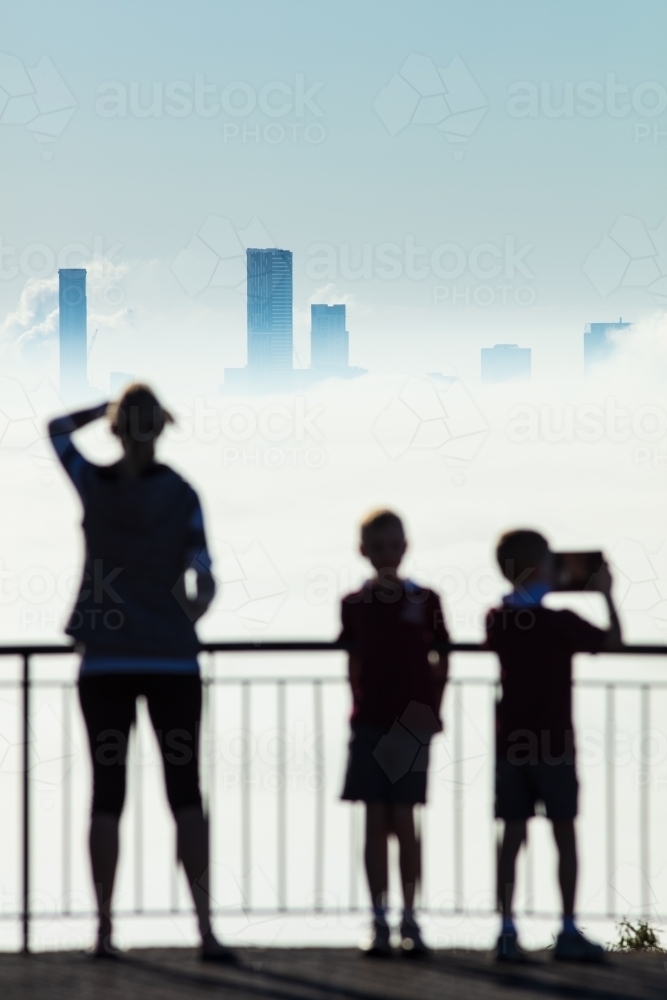 Silhouetted female and two boys standing at the viewing platform of The Summit at Mount Coot-tha. - Australian Stock Image