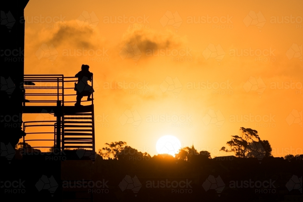 Silhouetted girl watching the sun set from stairs - Australian Stock Image