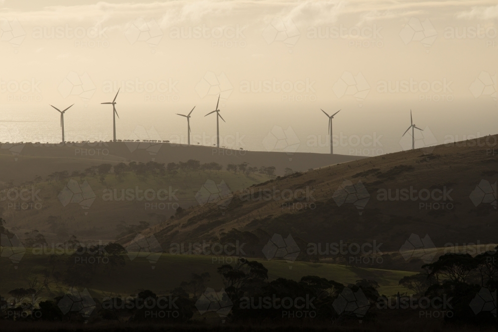Silhouetted row of wind turbines on a hill in a paddock - Australian Stock Image
