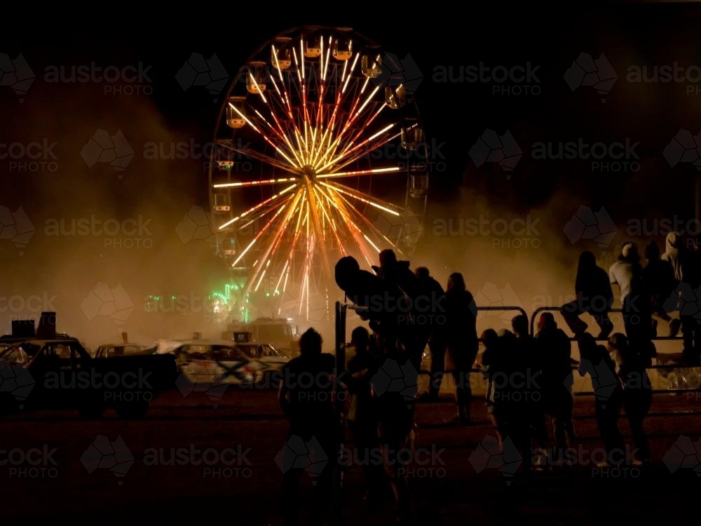 Silhouetted spectators watching a demolition derby with ferris wheel - Australian Stock Image