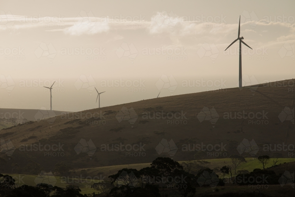 Silhouetted wind turbines on a hill in a paddock - Australian Stock Image
