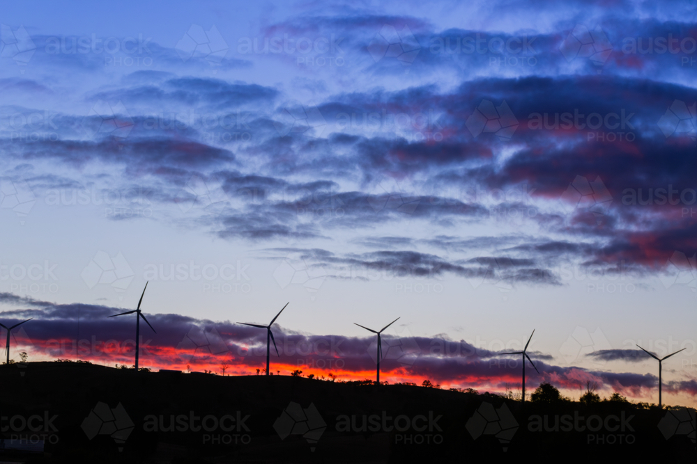 silhouetted wind turbines power generators on ridgeline at dusk after sunset - Australian Stock Image