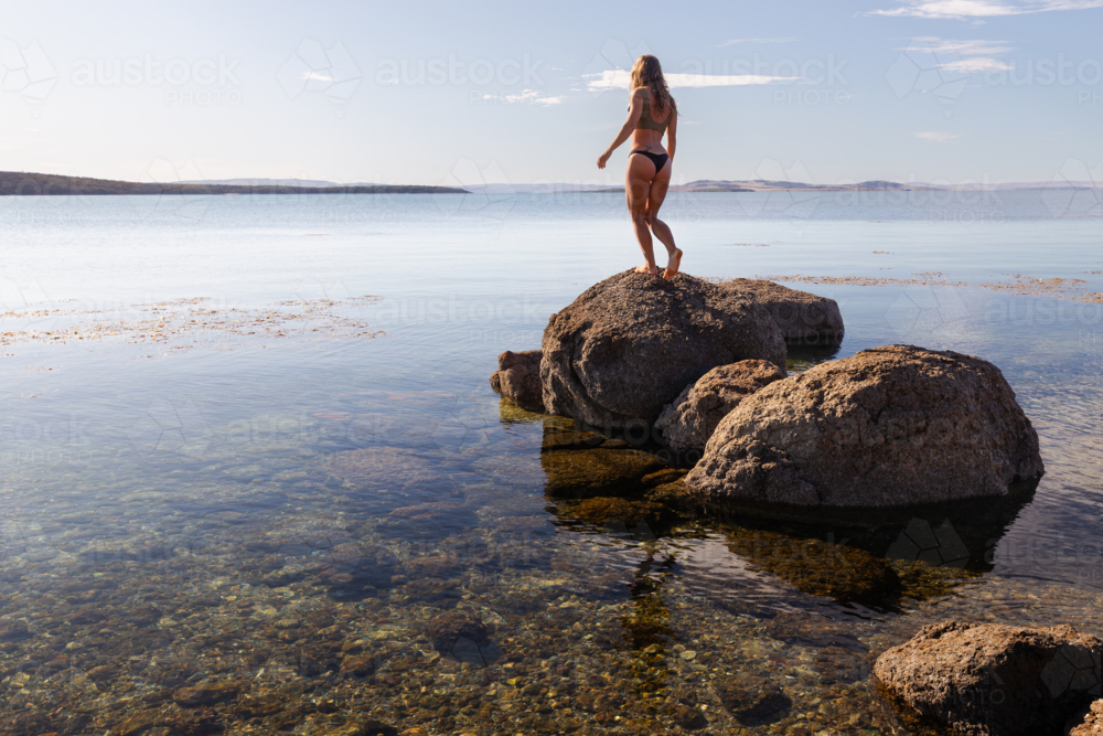 Silhouetted woman in bikini exploring calm coastline during summer in South Australia - Australian Stock Image