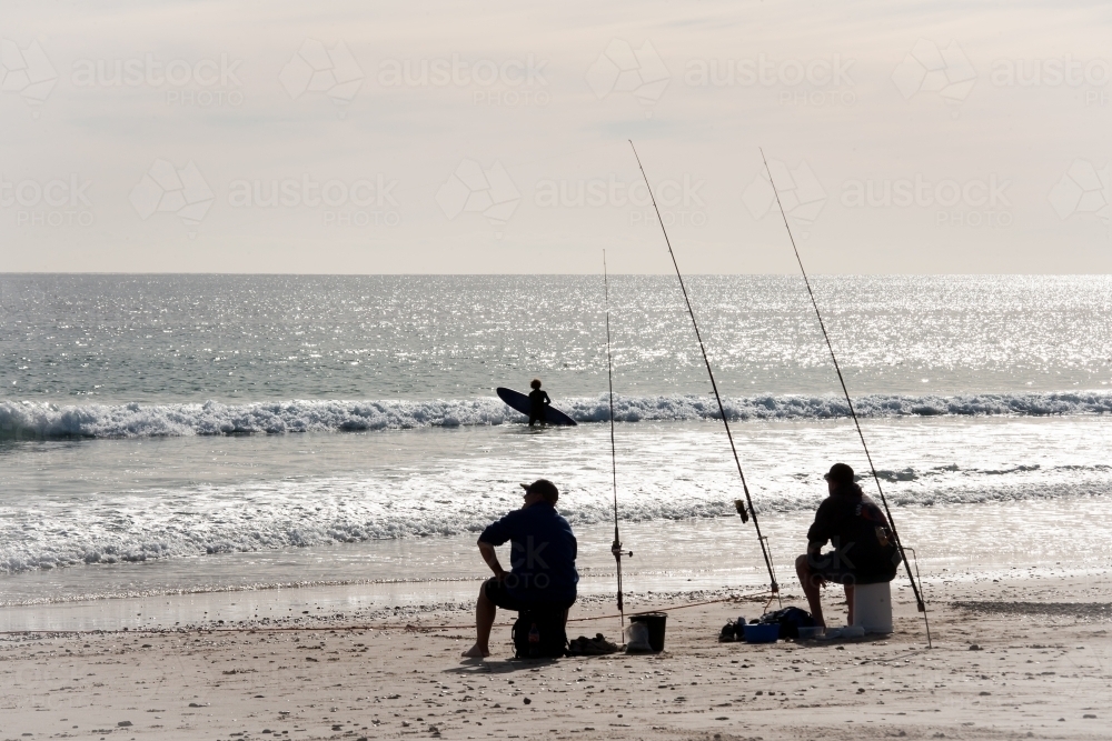 Silhouettes of fishermen and surfer at a regional beach - Australian Stock Image