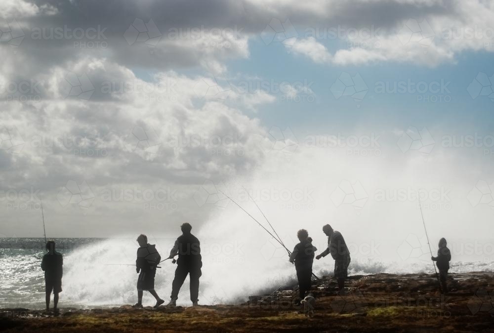 Silhouettes of people fishing off the beach with big waves - Australian Stock Image