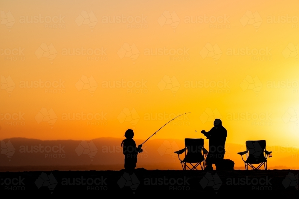 silhouettes of people fishing on the beach at sunset - Australian Stock Image