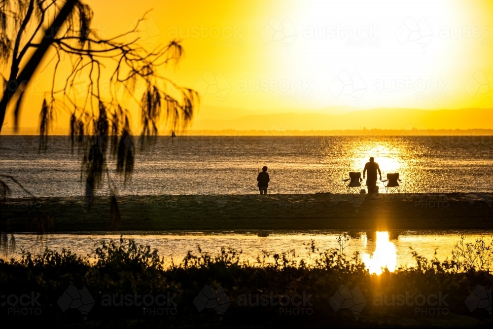 silhouettes of people fishing on the beach at sunset - Australian Stock Image