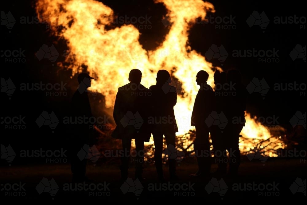 Silhouettes of people standing around a bonfire - Australian Stock Image