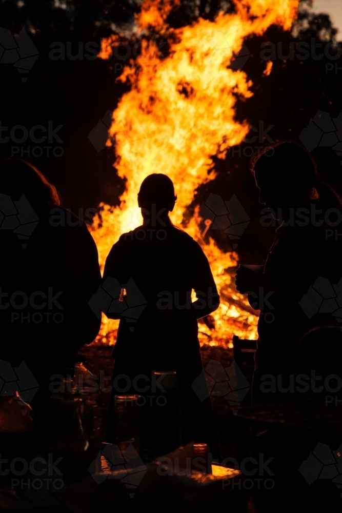 Silhouettes of three people standing around a table near a bonfire - Australian Stock Image