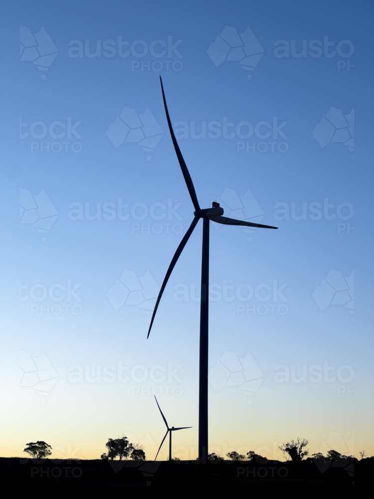 silhouette of wind turbine at dusk with another turbine behind and gum trees on the horizon - Australian Stock Image