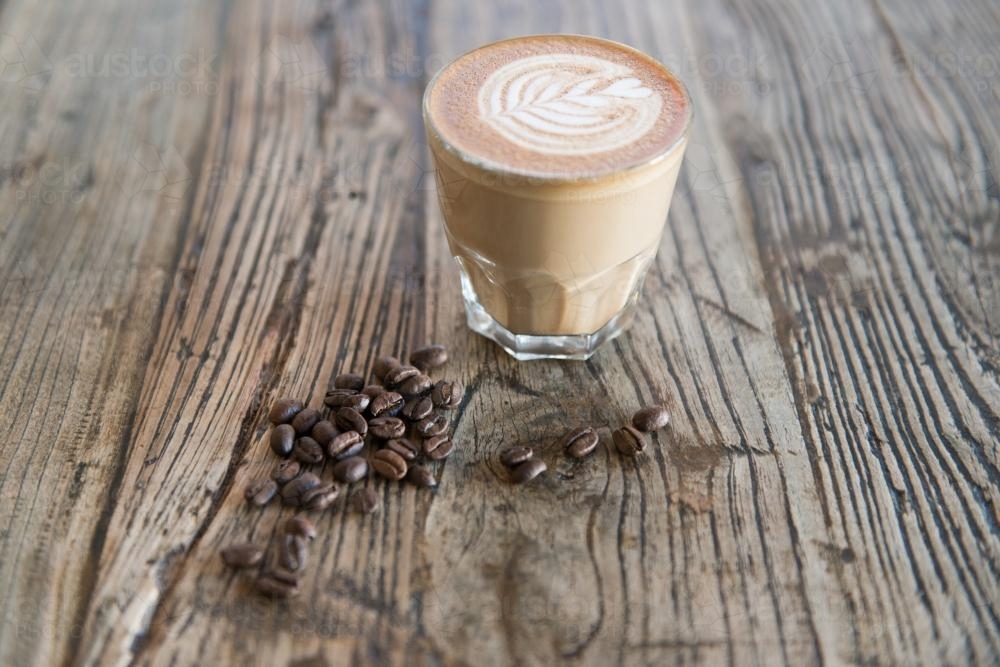 Single latte sitting on a wooden table with scattered coffee beans - Australian Stock Image