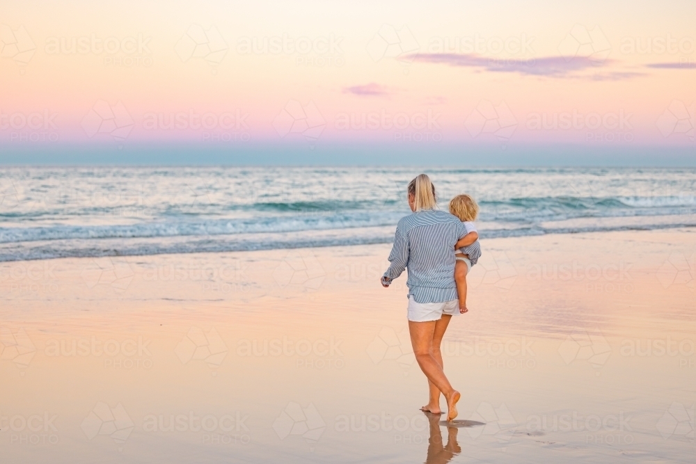 Single mother carrying son on the beach in twilight light. Sunset on the Gold Coast - Australian Stock Image