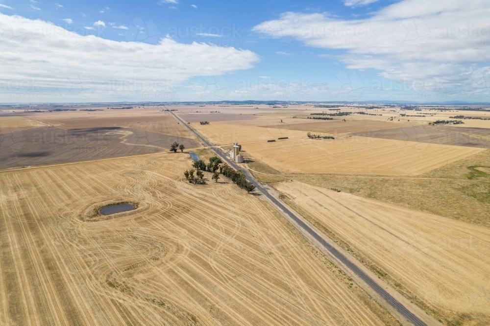 Single road leading into distance with silo and grain storage viewed below. - Australian Stock Image