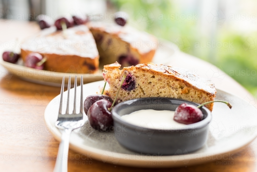 Single slice of cherry cake with icing dusting, cream and cherries on the side - Australian Stock Image