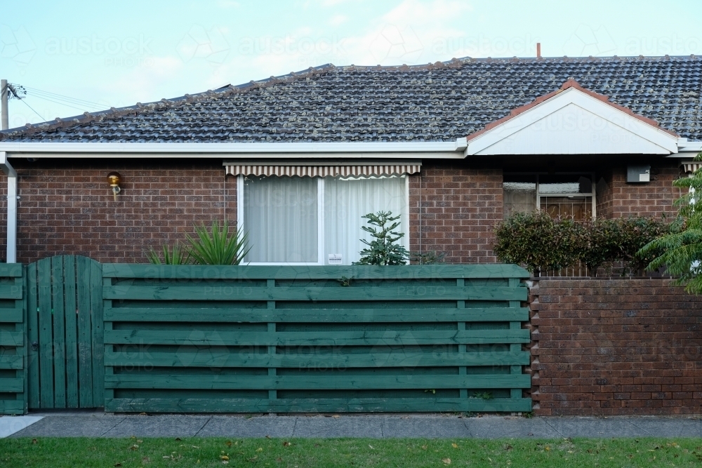 Single storey brick house with green fence - Australian Stock Image