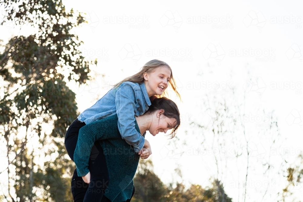 Sister giving her younger sibling a piggyback ride - Australian Stock Image