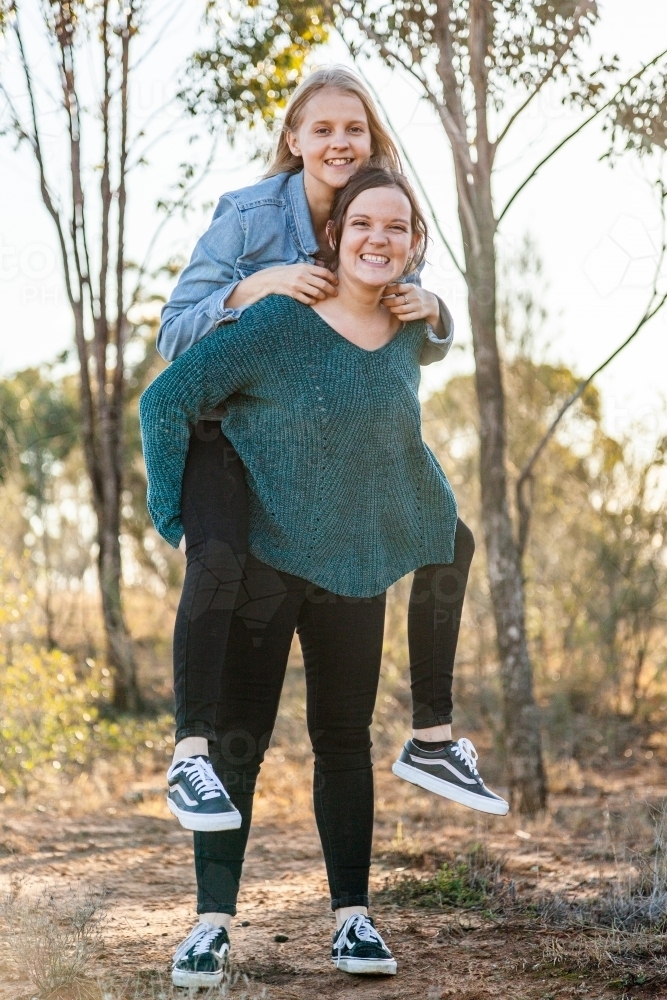 Sister giving her younger sibling a piggyback ride - Australian Stock Image