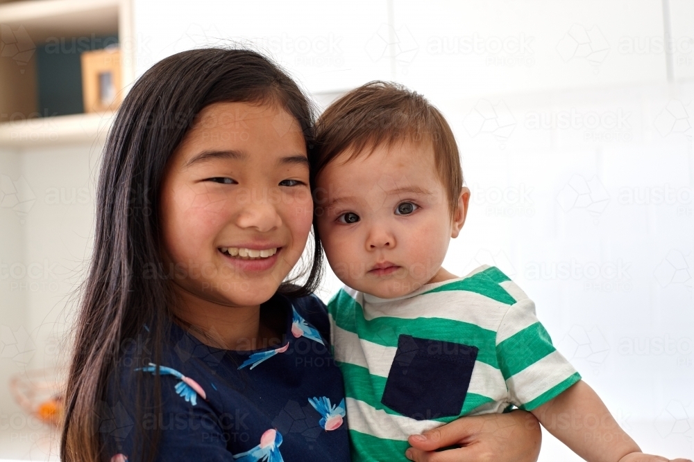 Sister holding younger baby brother in kitchen - Australian Stock Image