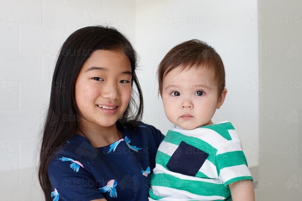 Sister holding younger baby brother in kitchen - Australian Stock Image