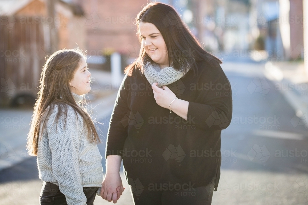 Sisters holding hands talking to each other and smiling - Australian Stock Image