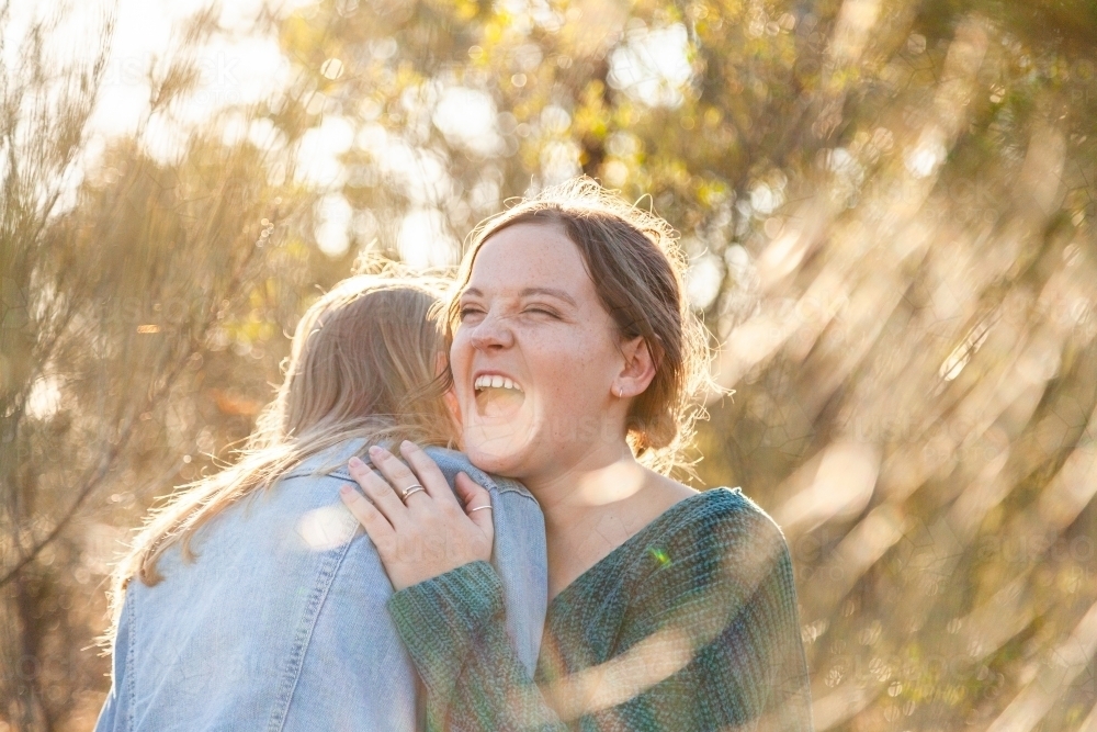 Sisters laughing together and giving one another a hug - Australian Stock Image