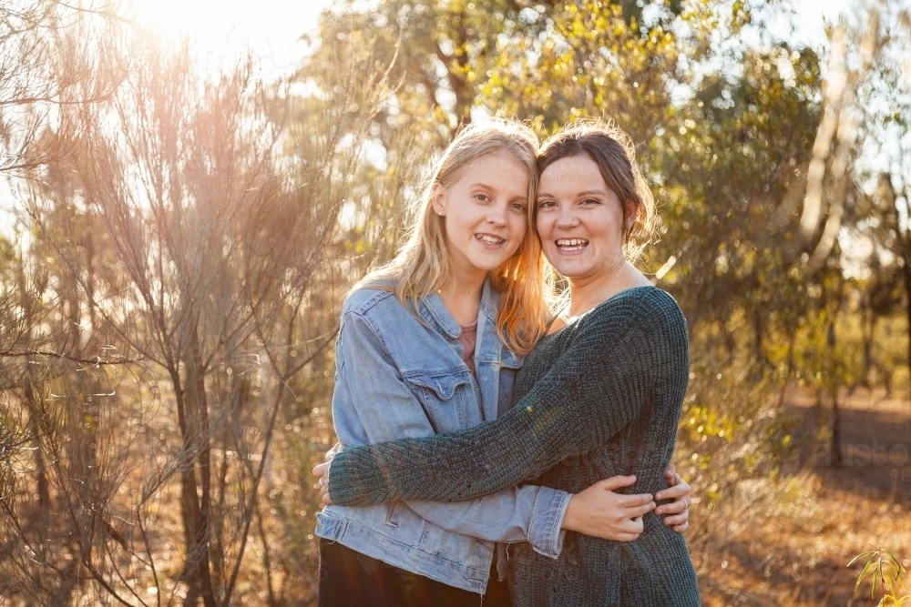 Sisters laughing together and giving one another a hug - Australian Stock Image