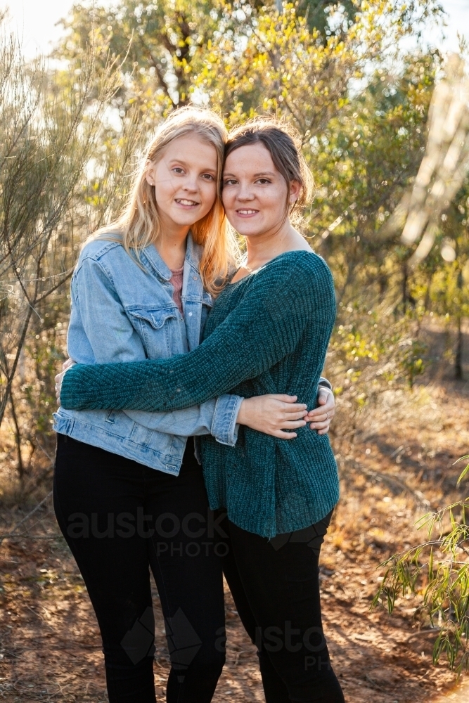 Sisters laughing together and giving one another a hug - Australian Stock Image