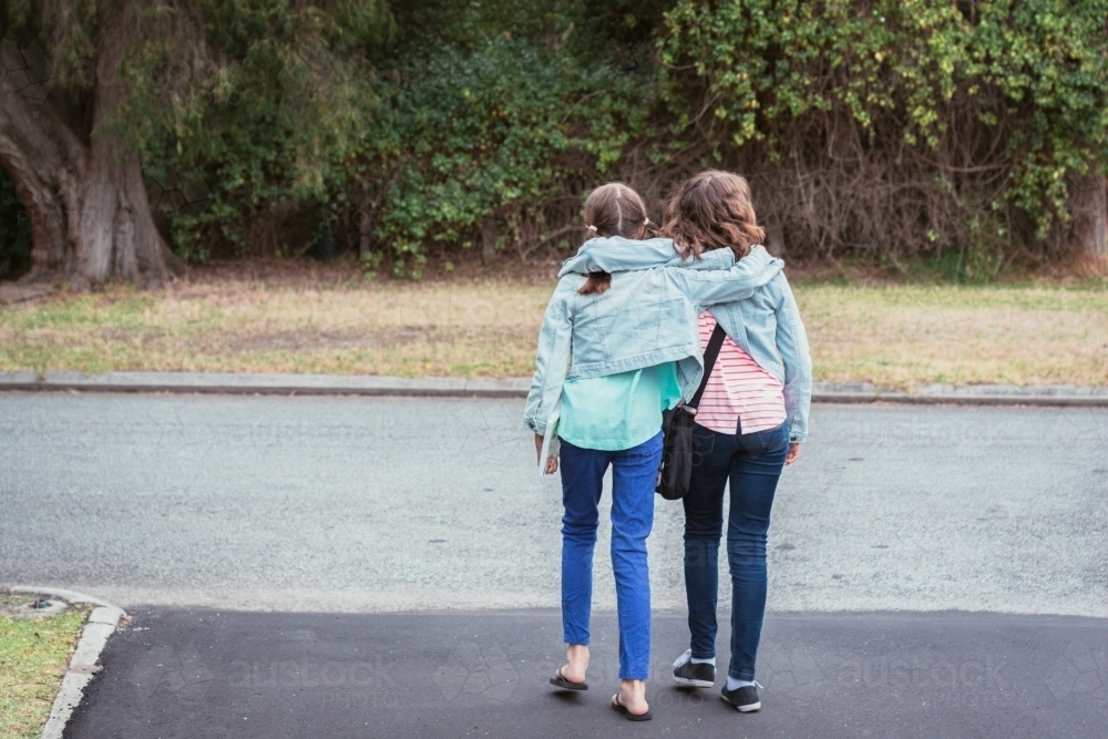 sisters or friends walking along hugging - Australian Stock Image
