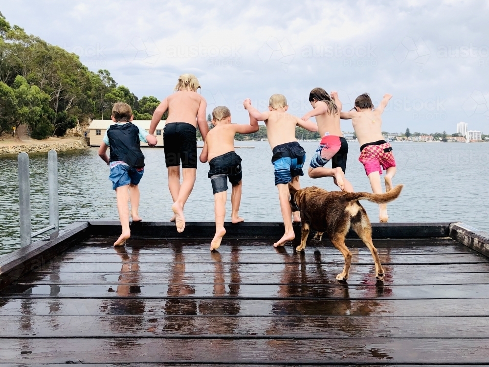 Six kids holding hands as they jump off a wharf into the water - Australian Stock Image