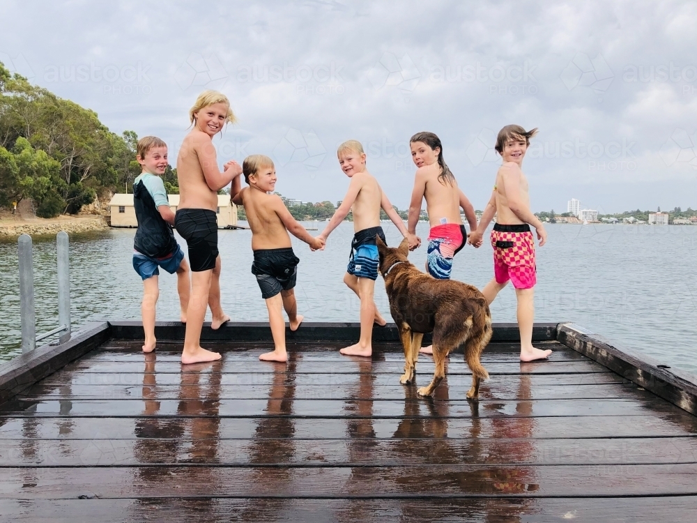 Six kids holding hands smiling at camera, about to jump of a pier - Australian Stock Image