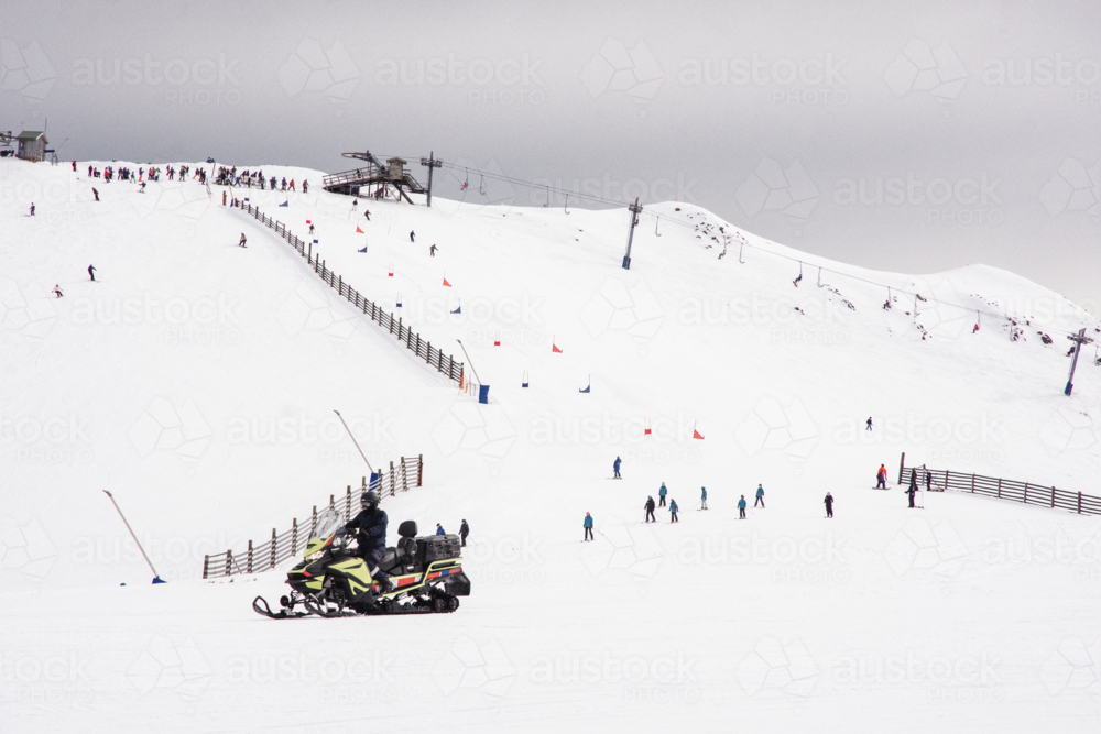 Skiiers on mountain with ski lift and race course, with ski-doo in foreground Mt Buller, Victoria - Australian Stock Image