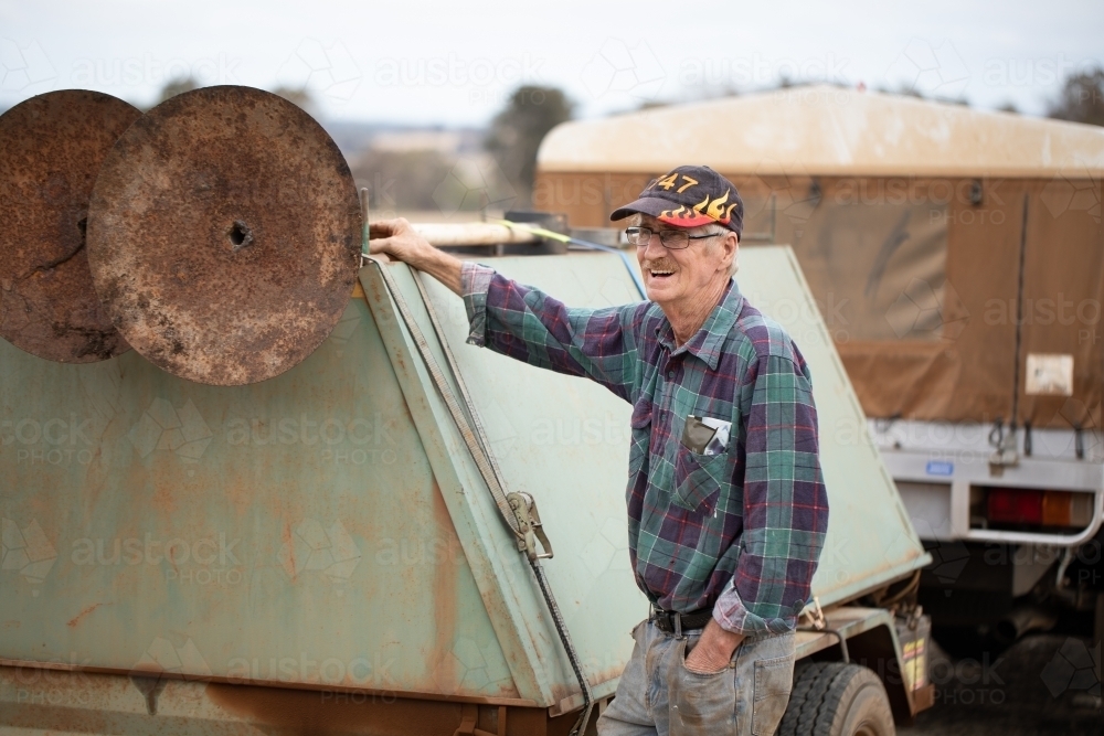 skinny old man outdoors near tradesman's trailer - Australian Stock Image