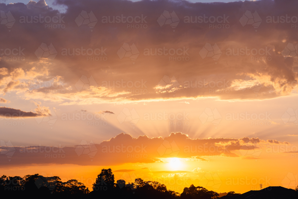 Skyscape of golden rays of sunlight from behind clouds floating in sky at sunrise - Australian Stock Image