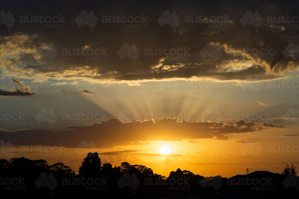Skyscape of sun with golden rays of light from behind clouds at sunrise - Australian Stock Image