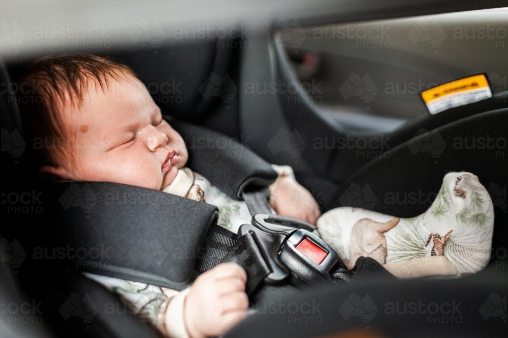 sleepy newborn baby strapped into car seat - safety - Australian Stock Image