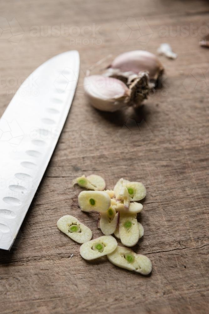 sliced garlic on a wooden board, with knife - Australian Stock Image