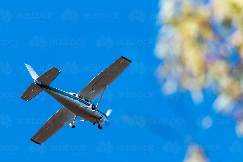 small aeroplane flying over against blue sky - Australian Stock Image