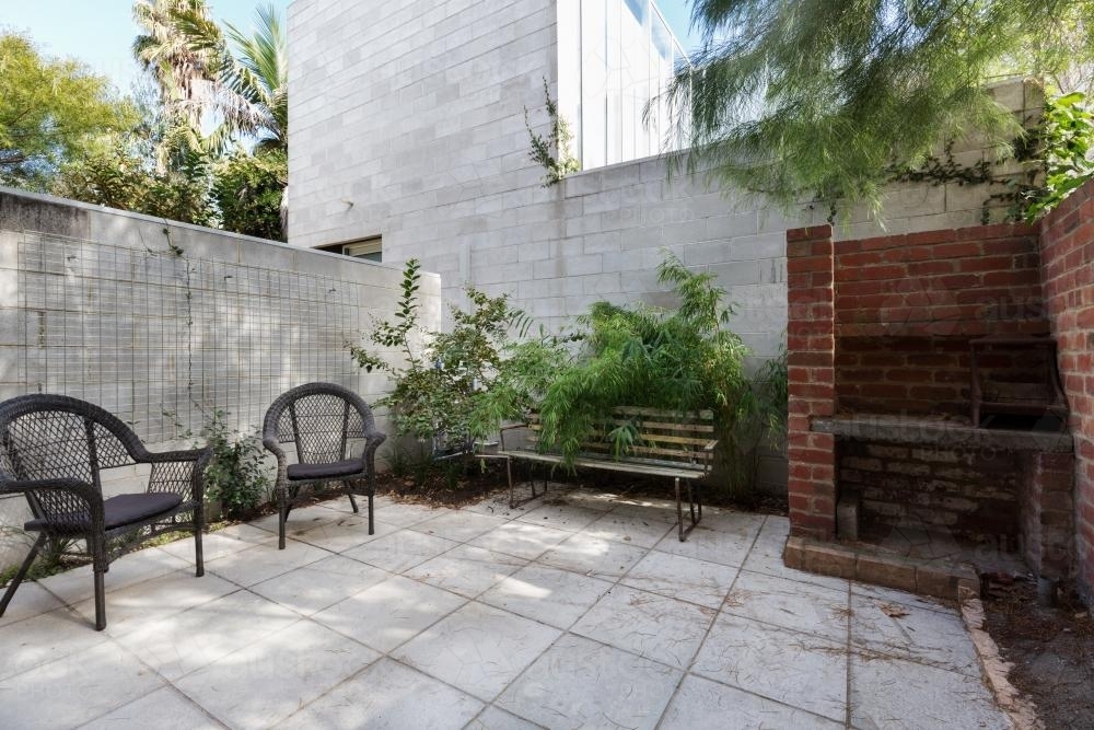 Small apartment courtyard with paving and cane outdoor chairs - Australian Stock Image