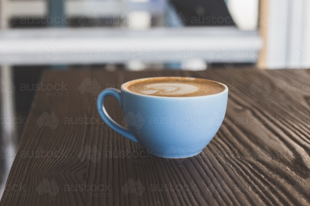 Small blue cup of coffee sitting on a wooden table at a cafe - Australian Stock Image