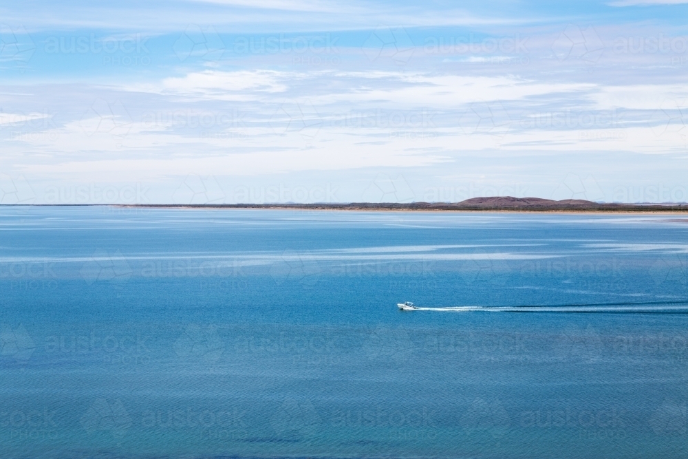 small boat heading out to sea across a calm bay - Australian Stock Image