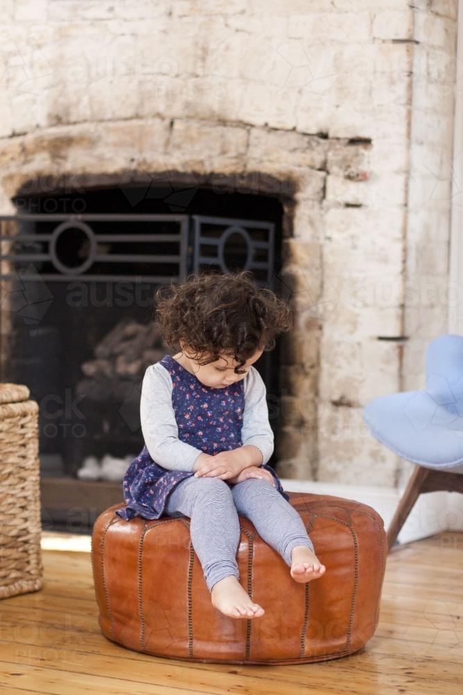 Small child sitting on round leather ottoman - Australian Stock Image