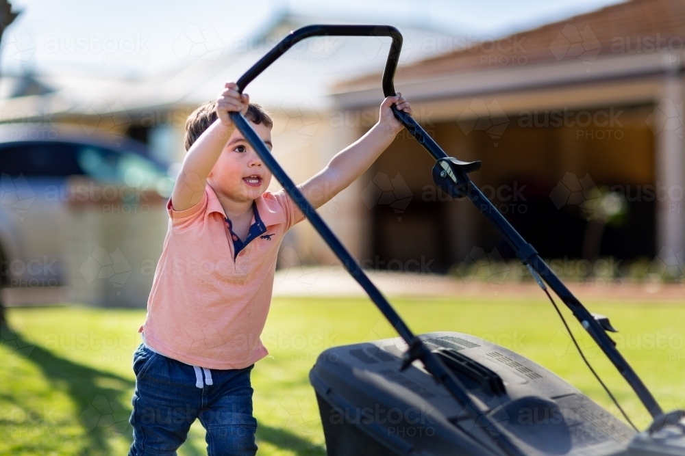 Small child trying to push lawnmower - Australian Stock Image