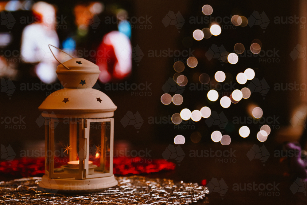 Small indoor lantern with Christmas tree in background creating bokeh light effect - Australian Stock Image