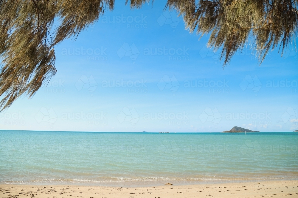 Small island off the coast in the Whitsundays framed by trees - Australian Stock Image