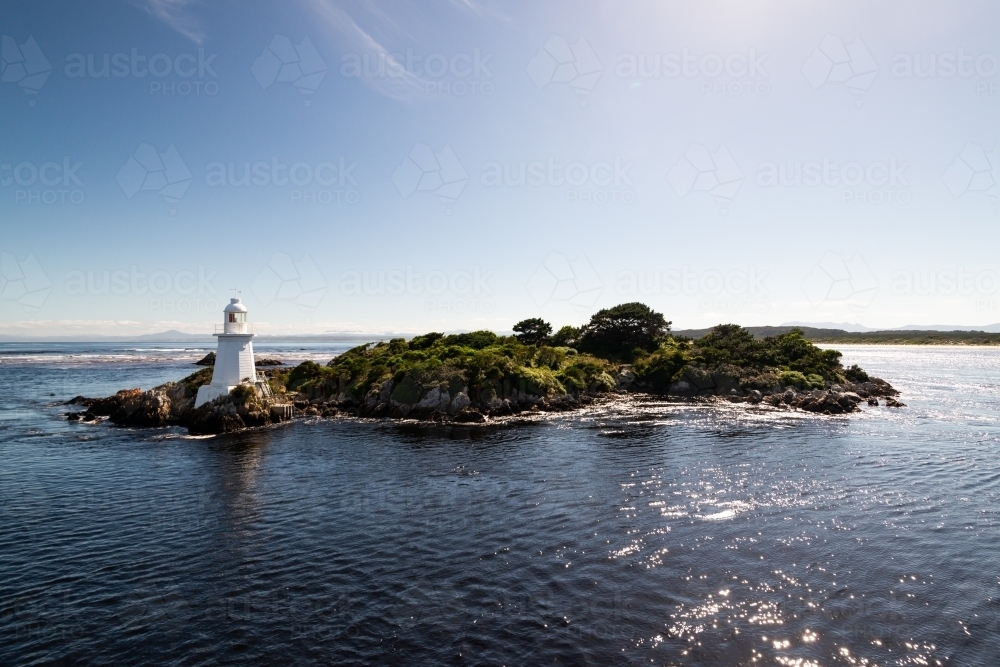 Small island with a cute little lighthouse, blue sky and bluewater. - Australian Stock Image