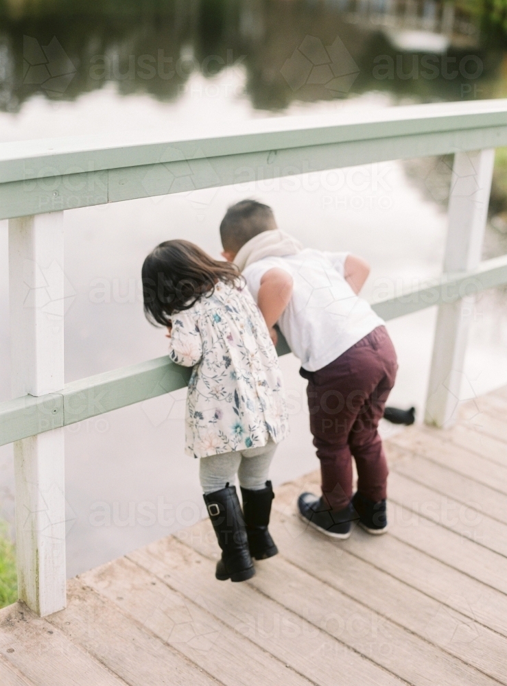 Small kids on footbridge, looking over the fence into the water below - Australian Stock Image