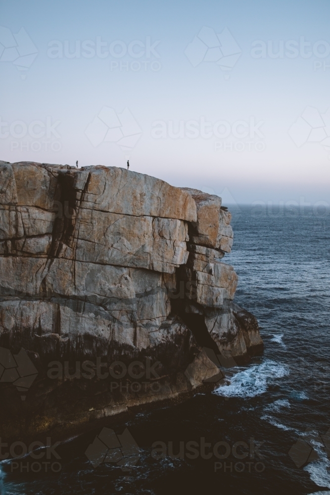 Small people on huge rock formation at sunset - Australian Stock Image