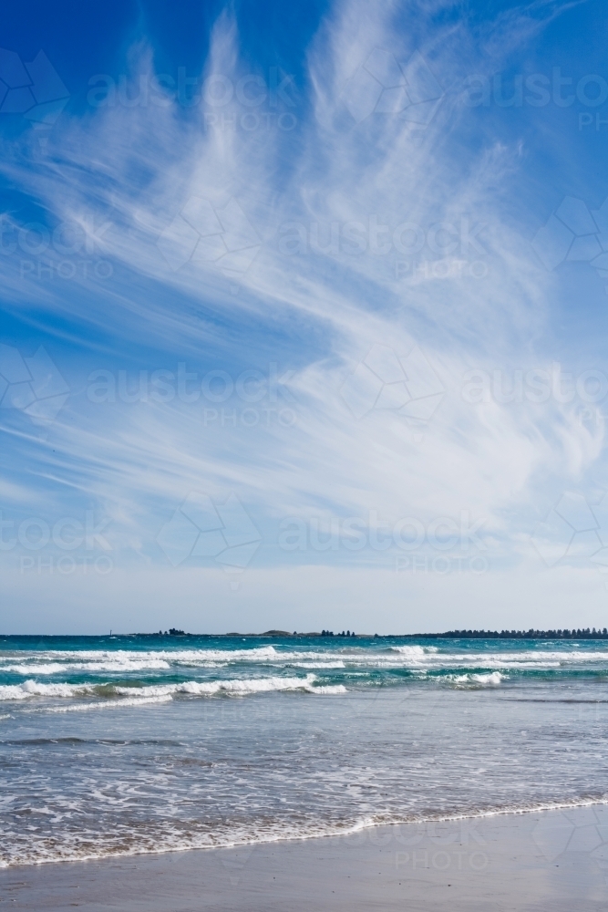 small waves breaking on a beach under a big sky - Australian Stock Image