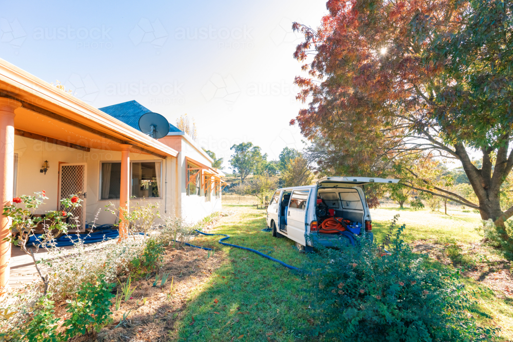 Small white van with commercial carpet steam cleaning equipment parked outside home with blue hoses - Australian Stock Image