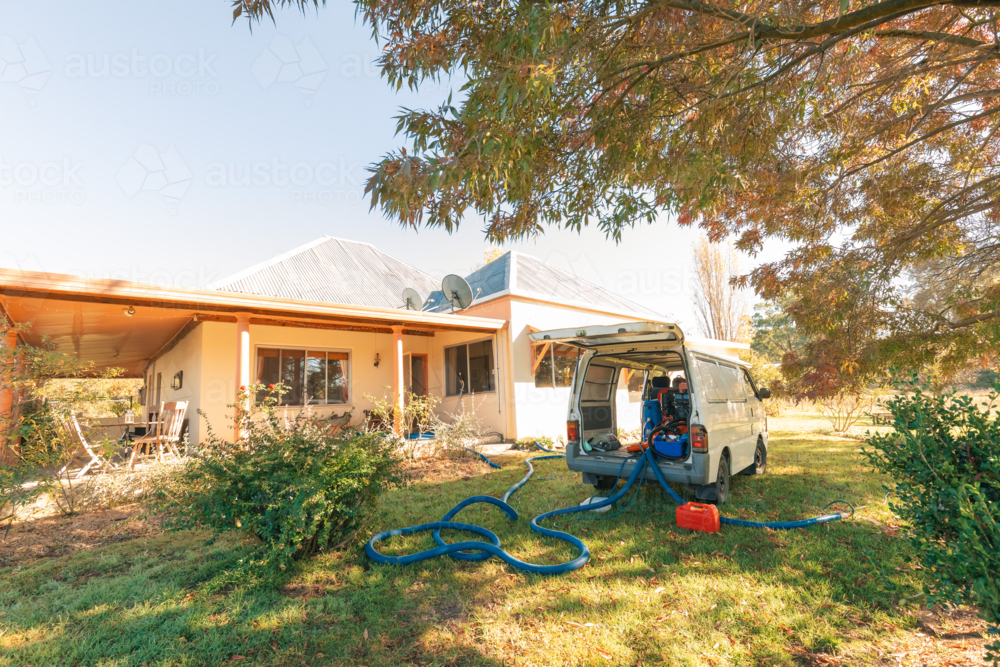 Small white van with commercial carpet steam cleaning equipment parked outside home with hoses - Australian Stock Image